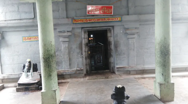 A sanctum doorway with a Tamil name board above it, seen between two green pillars, with a Nandi at the left.