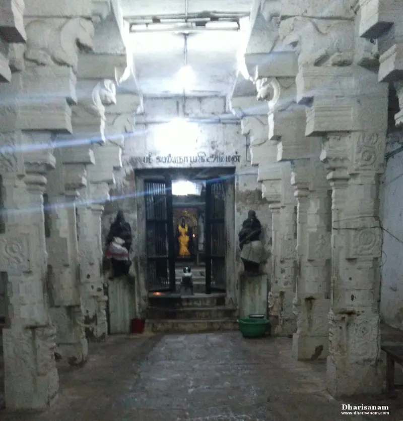 Stone pillars line a hall; at the far end an iron gate opens to a shrine with a yellow-clad image.