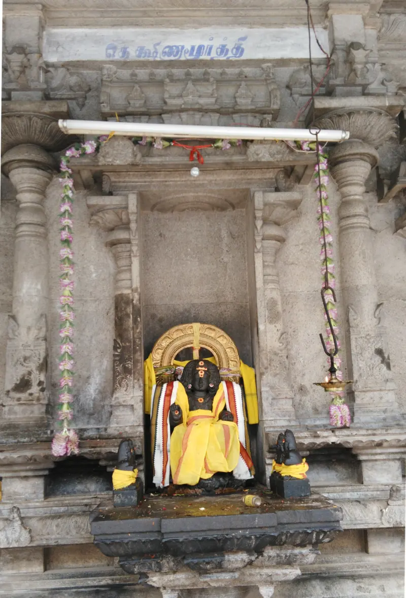 A seated black stone image in yellow cloth in a niche, with garlands hanging on either side