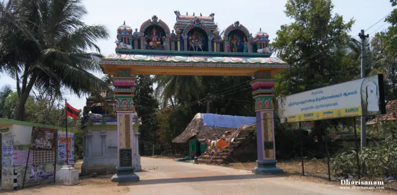 A painted arch with sculpted figures spans the road between two pillars; a signboard and trees stand beside it.