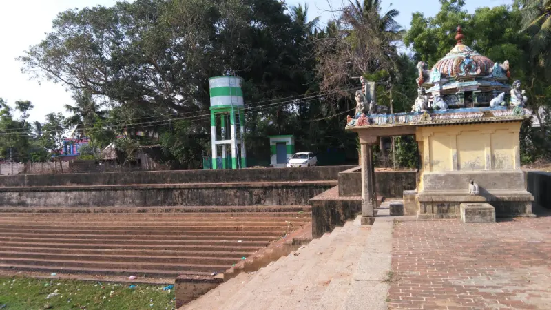 Wide brick steps lead down to water, with a small mandapam topped by a painted crest at the right