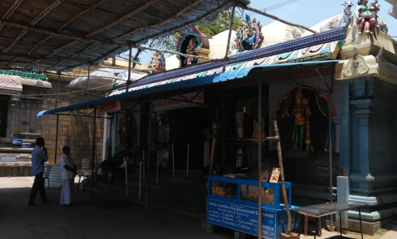 A shrine front covered by a blue canopy, with a painted idol in a niche and two men standing at the left