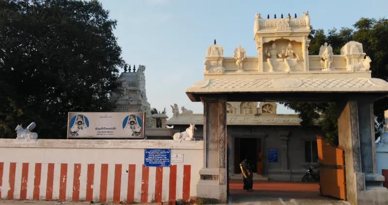 A white stone gateway with sculpted figures beside a red and white striped wall and a signboard.