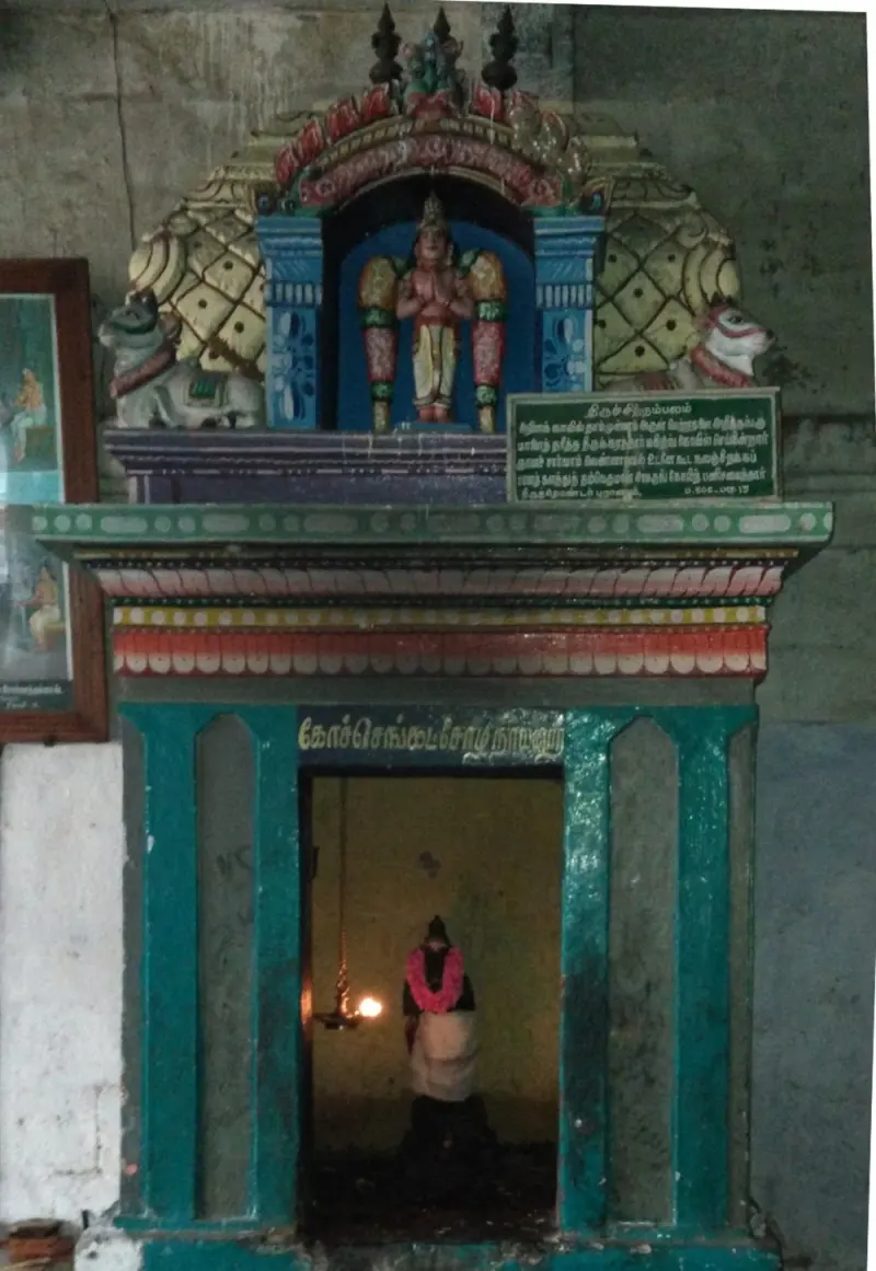A shrine entrance with a painted standing figure above it and a person inside by a lamp.