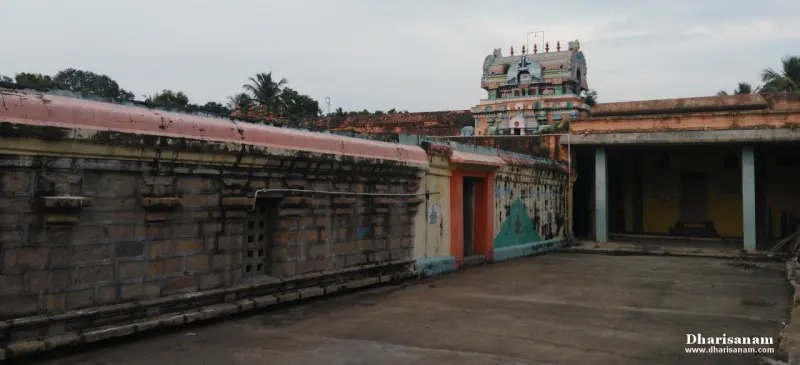 A long stone corridor wall with a painted tower rising behind it and an open pillared hall to the right.