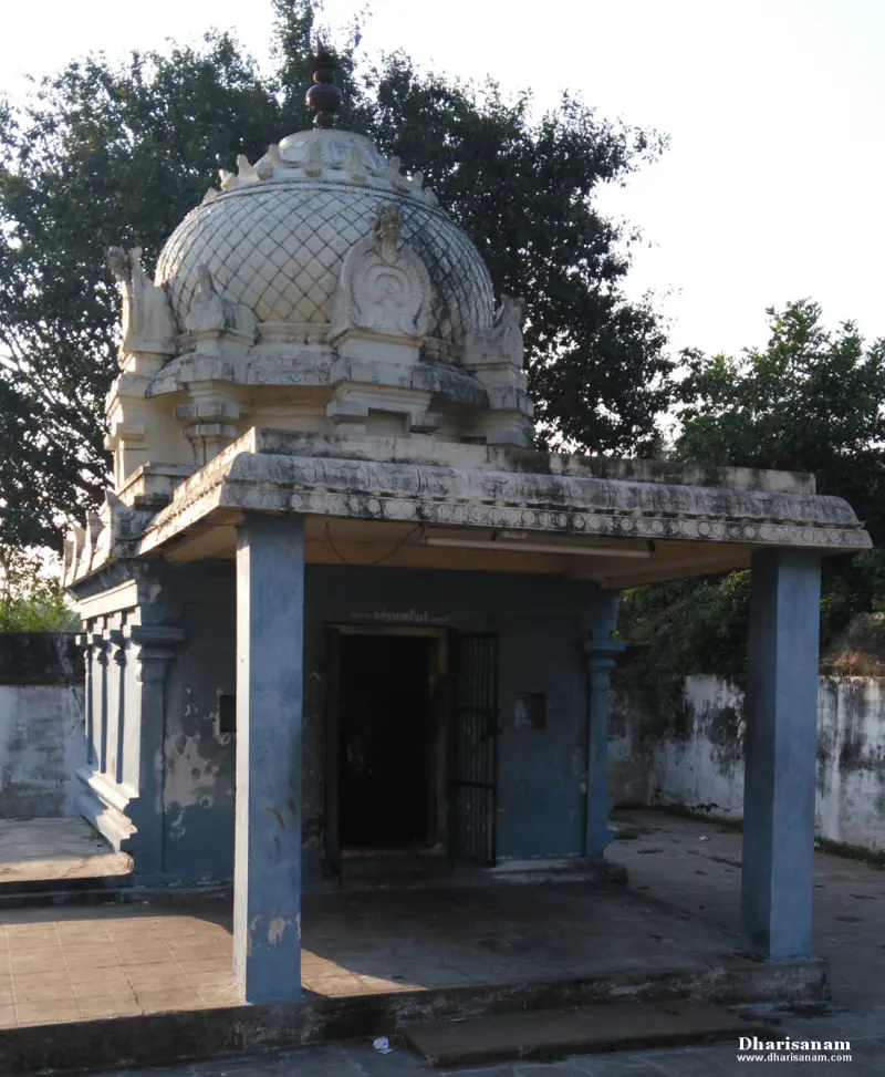 A small blue-grey shrine with a lattice-patterned dome, pillars in front and trees behind