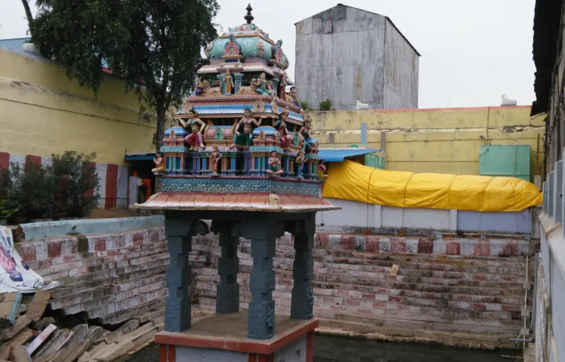 A small pillared shrine with a painted tower top beside a stepped tank