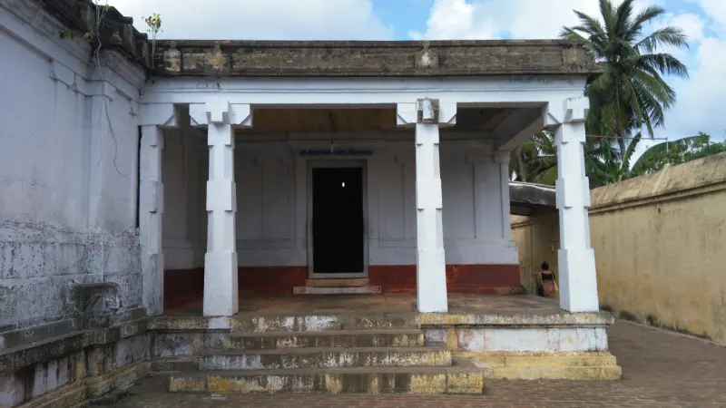 A small white pillared shrine with a dark doorway, set against a corridor wall