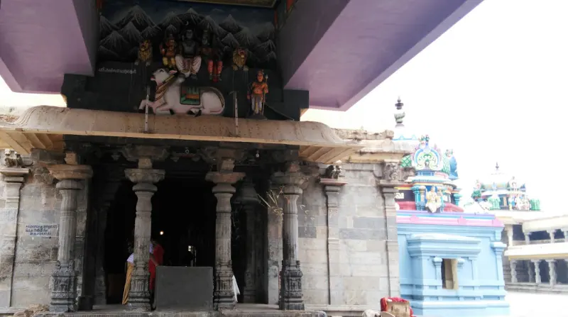 A stone pillared entrance with a painted sculpture of Shiva and a bull above it, and a blue shrine beside
