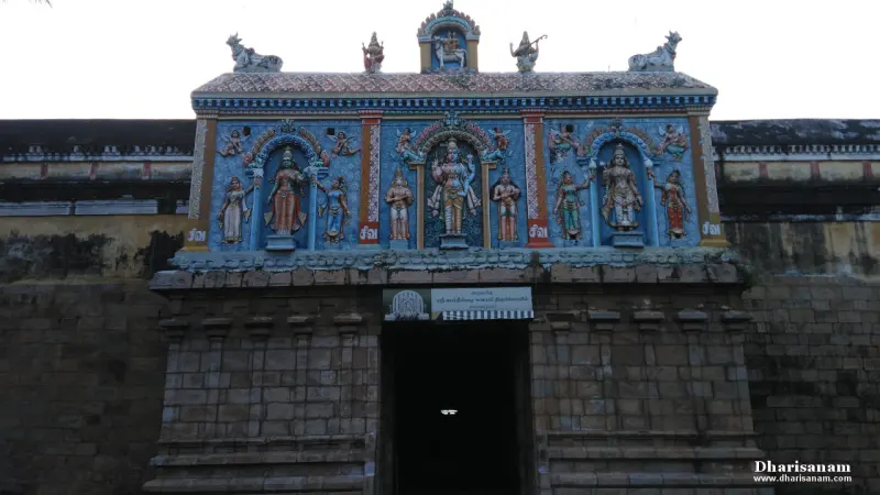 A stone gateway topped by a blue panel with painted figures of deities, and a dark entrance below