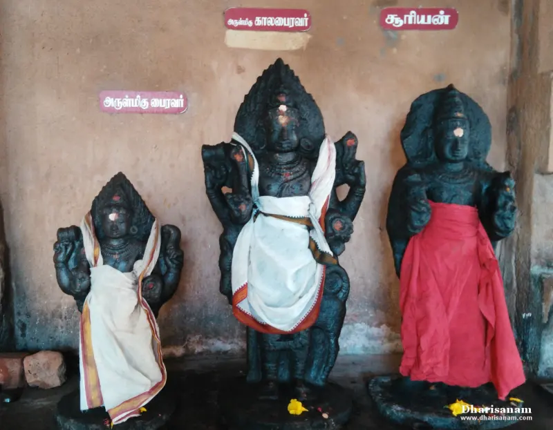Three black stone idols in a row, each with a Tamil name board above, dressed in white and red cloth