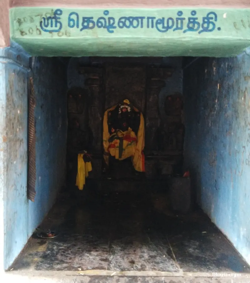 Small blue-walled niche with a Tamil name board above an idol draped in yellow cloth
