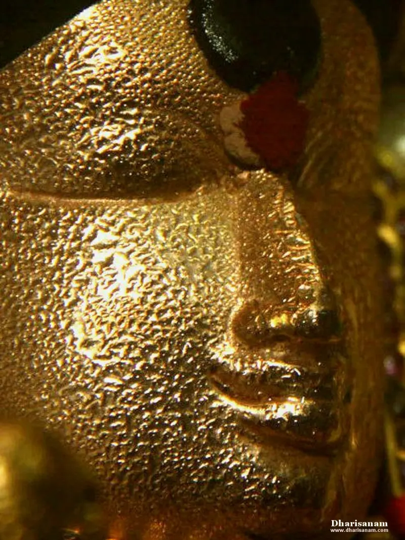 Close view of a golden face with closed eyes and a red mark on the forehead, its surface dotted with droplets