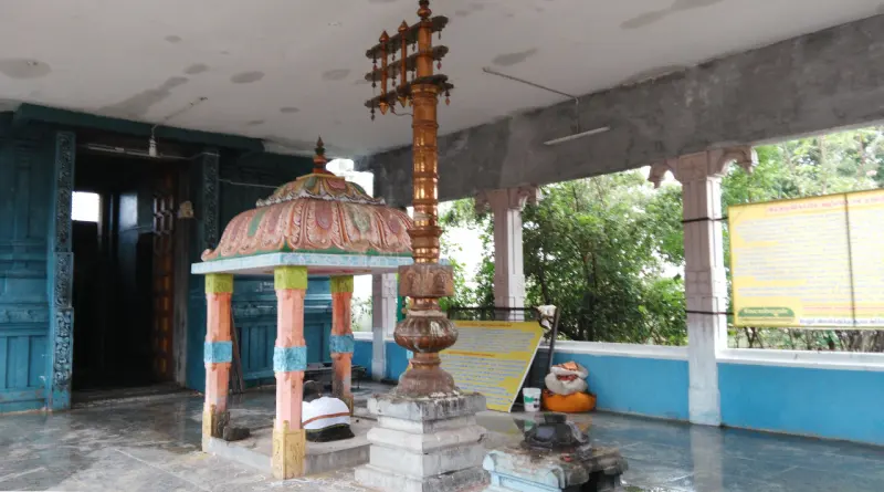 A tall copper flagstaff beside a small domed pavilion in a covered hall with blue walls.