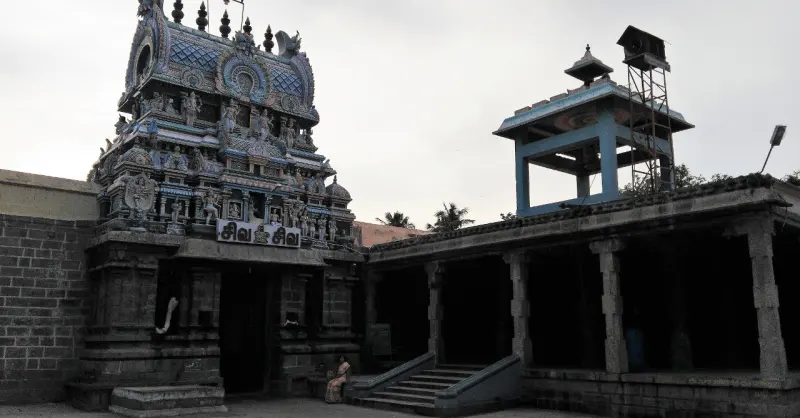 A painted tower over a gateway with a name board, and a pillared hall with steps on the right