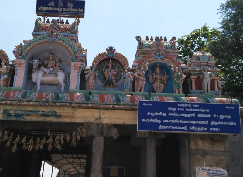 Colourful stucco figures of deities above an entrance, with a blue name board in Tamil