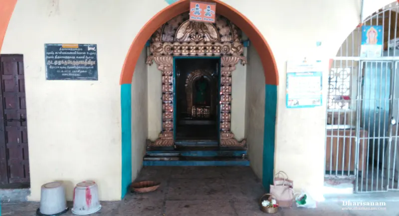 A carved metal doorframe in a small arched recess, with a Tamil plaque on the wall to its left.