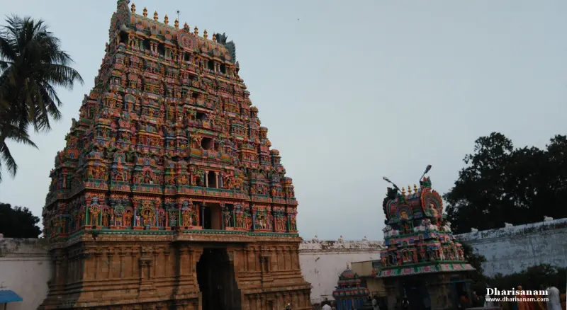 A tall gopuram in stone and colour beside a smaller tower, with a palm tree at left
