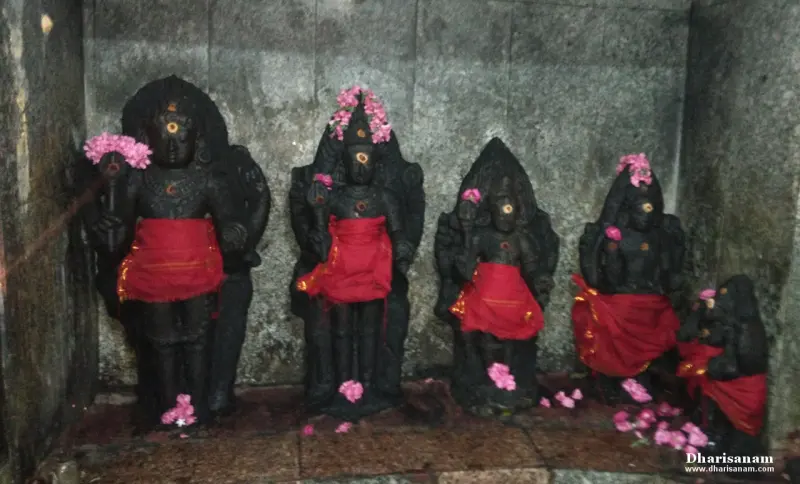 Five black stone idols draped in red cloth with pink flowers