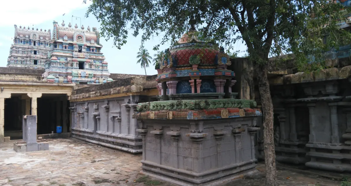 A domed shrine in a stone courtyard, the tall gopuram rising behind it