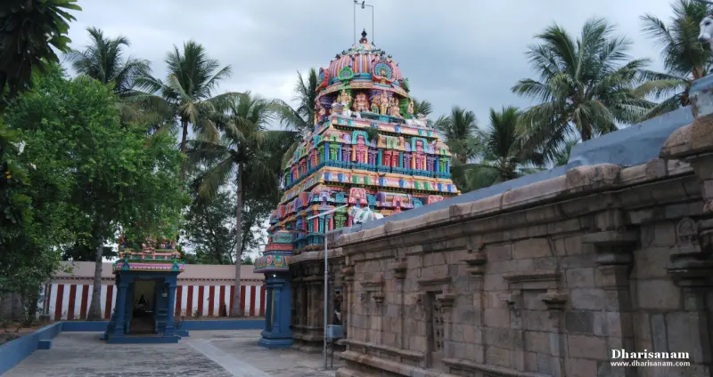 A colourful tower over the stone corridor wall, palm trees behind and a small blue shrine at the left