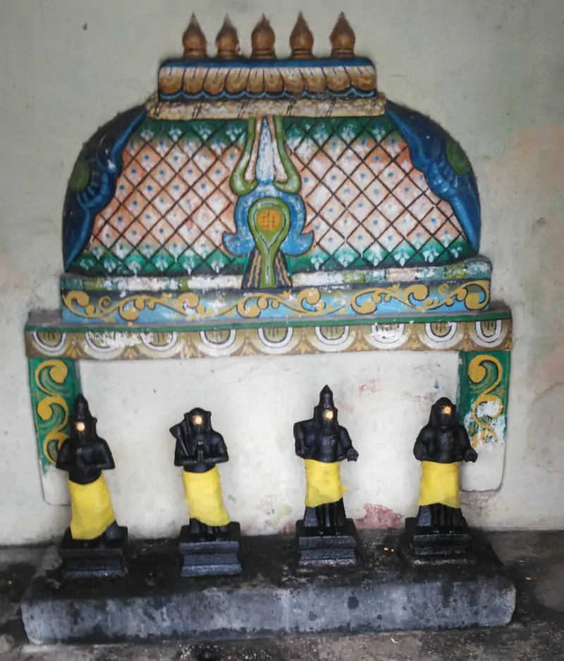 Four small black idols in yellow cloth stand in a row beneath a painted niche.