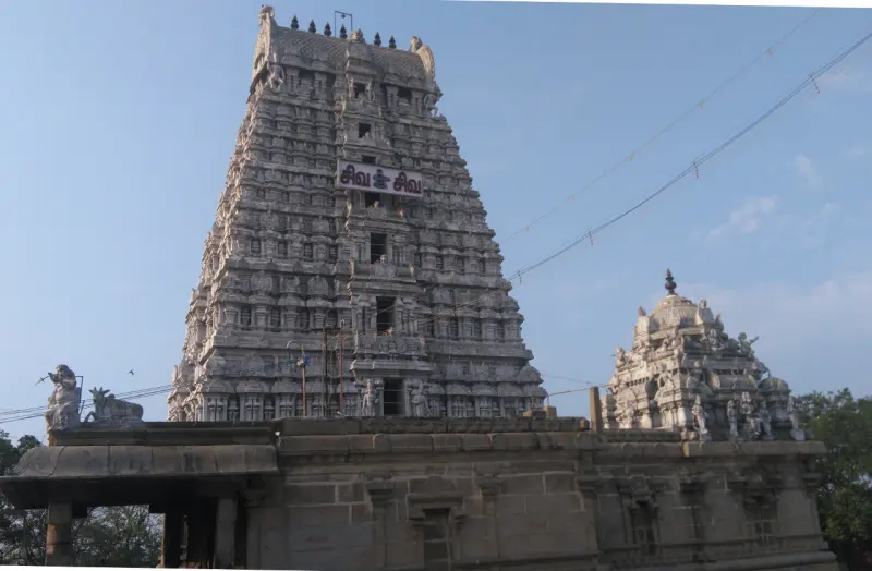 A tall carved gopuram under a clear sky, with a smaller domed shrine tower beside it