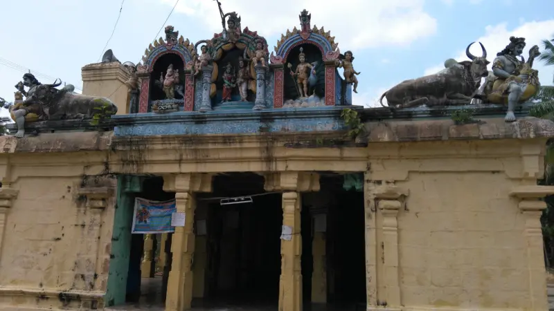 A yellow-walled mandapam with painted figures and two bulls on the roof, and dark pillared openings below.