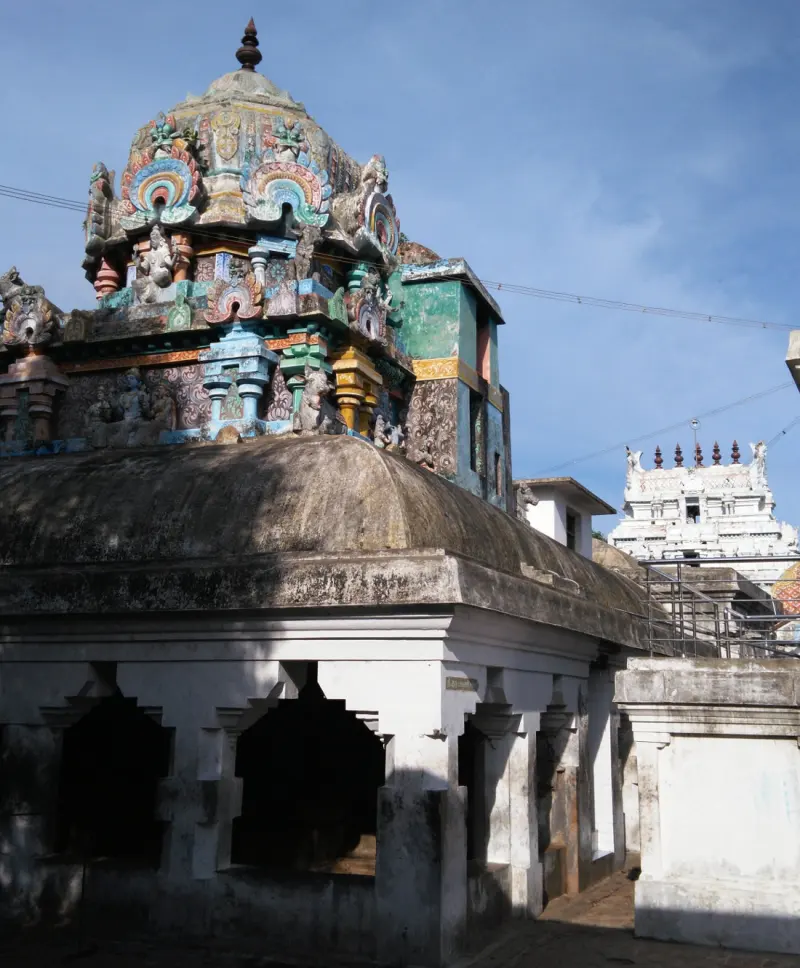 A colourful shrine tower with sculpted figures rising above a plain corridor roof, with the Rajagopuram behind.