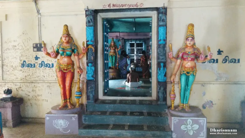 Two painted guardian figures flank steps up to the shrine door; a devotee sits inside