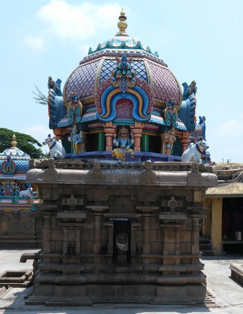 A stone shrine with a small doorway, topped by a colourful dome with white bull statues, in the courtyard