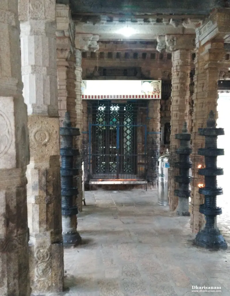 Carved pillars and dark metal lamp stands in a hall, leading to a grilled doorway ahead