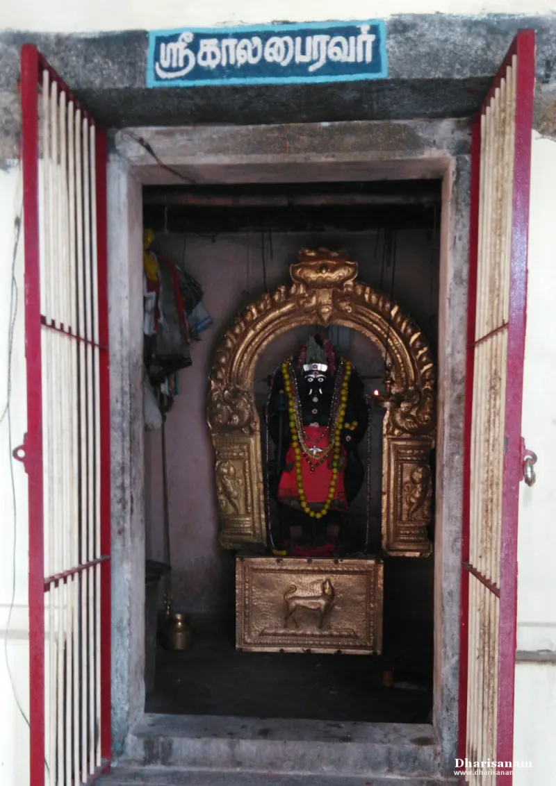 Small shrine with a garlanded black idol under a gilded arch, and a dog relief below