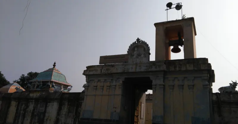 Stone gateway with a hanging bell on a small tower above, and a Nandhi on the wall