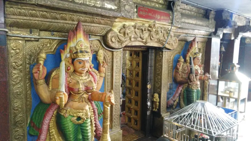 Two painted figures with weapons flanking a gilded door, with a lamp stand in front.