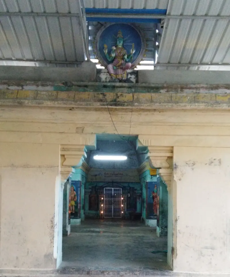 A painted seated goddess above a doorway; beyond it a hall leads to a lit, grilled sanctum entrance.