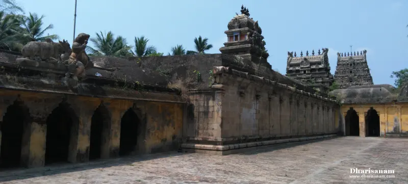 A paved corridor beside an arched wall, with two towers and a shrine tower against a blue sky