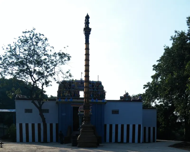 A tall flag post in front of a temple with striped walls and a tower behind it.