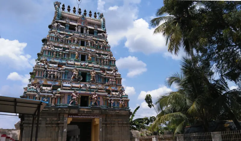 A tall tiered tower covered in painted stucco figures, with coconut palms beside it