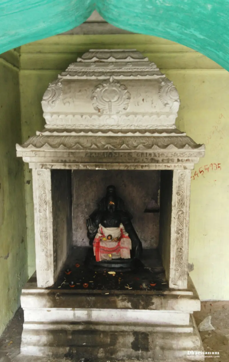 A black stone idol in red and white cloth seated inside a small white stone shrine