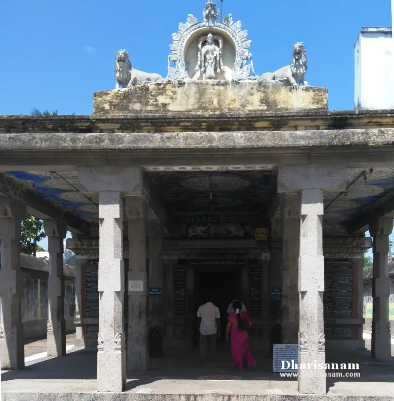 Stone hall with square pillars and a carved figure between two lions on the roof, devotees entering