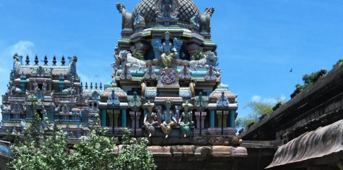 Two colourful temple towers with sculpted figures against a blue sky, seen over a stone wall.