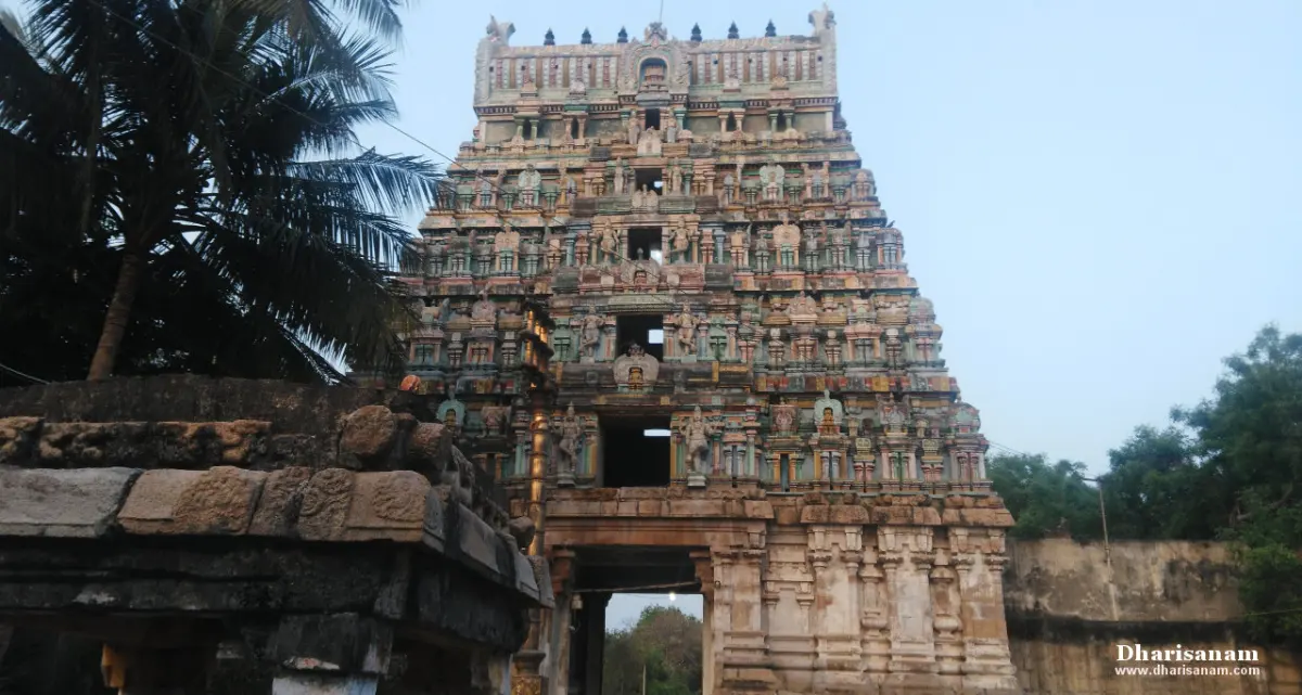 A tall tower with rows of painted figures, beside a stone wall and a palm tree.