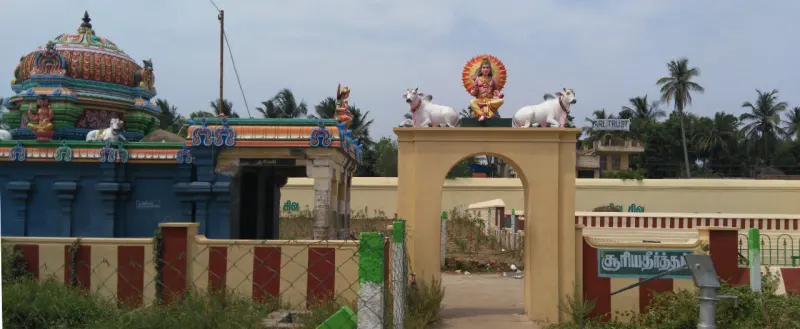 A yellow arch topped with a seated figure and two white bulls, with a green signboard reading Surya Theertham