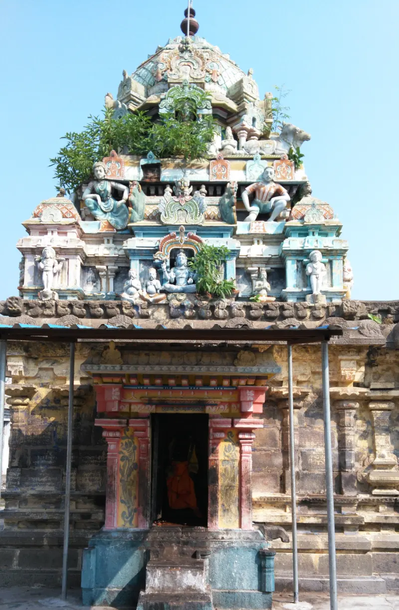 A painted tower with figures and plants growing on it, above a stone doorway with a red and yellow frame.