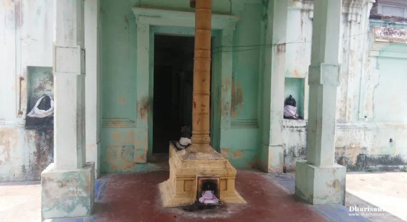 A tall wooden-coloured pillar on a stone base before a dark doorway, with small idols nearby.