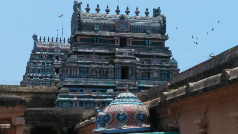 A tiered gopuram with its row of finials rising behind roofs, with a small painted dome in the foreground.