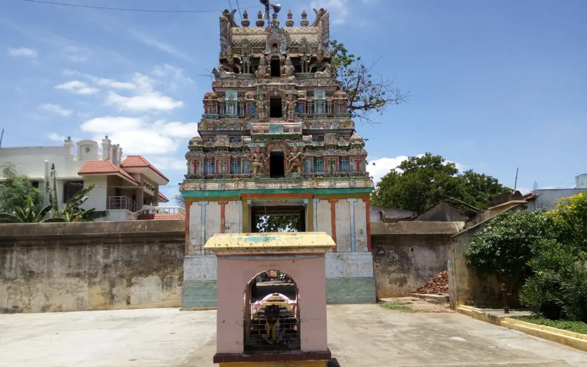 Painted tower rising behind a small pink shrine on an open paved courtyard
