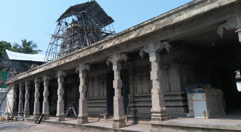 A long pillared corridor with scaffolding around the tower behind it