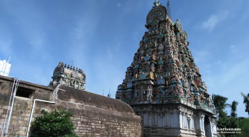 A tall tiered gopuram with painted figures, and a smaller tower beside a stone wall